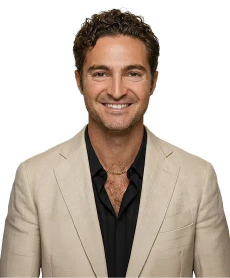 Smiling man with curly hair wearing a white blazer over a dark patterned shirt.